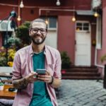 Lächelnder Mann mit Telefon in einem Straßencafé.