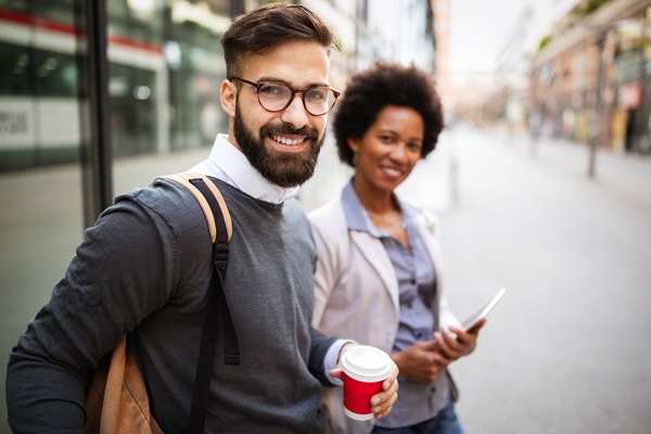 Zwei lächelnde Menschen im Freien mit Kaffee und Tablet.