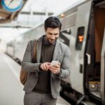 Hombre joven mira el celular mientras camina por una estación de metro.