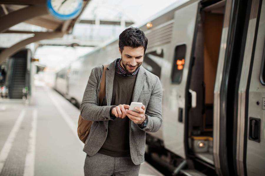 Hombre joven mira el celular mientras camina por una estación de metro.