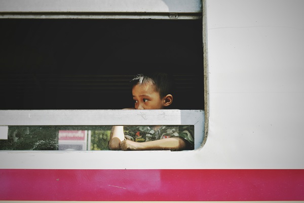 Desde afuera de un vagón de tren, se observa la cara de un niño que se asoma mientras mira hacia un lado de la imagen.