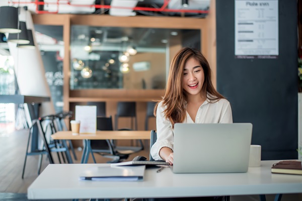 Mulher a trabalhar alegremente no computador portátil num café