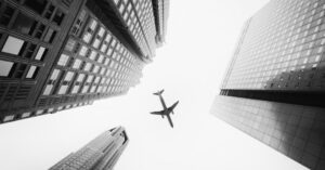 Airplane flying over skyscrapers in monochrome view.