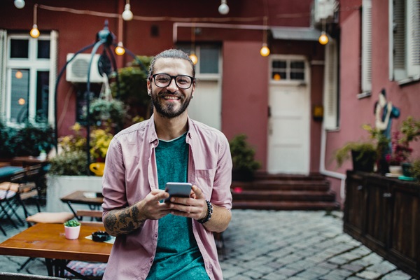 Smiling man holding phone in outdoor café.