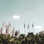 Milan Cathedral with surrounding flags and trees.