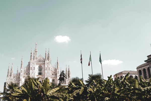 Milan Cathedral with surrounding flags and trees.