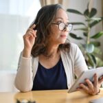 Woman with tablet, thinking at desk.