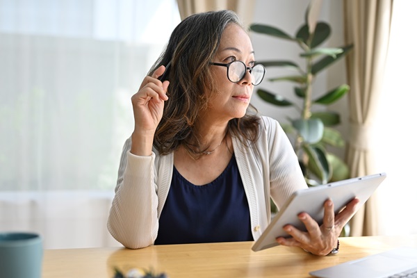 Woman with tablet, thinking at desk.